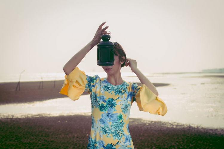 Young woman holding lantern while standing at beach