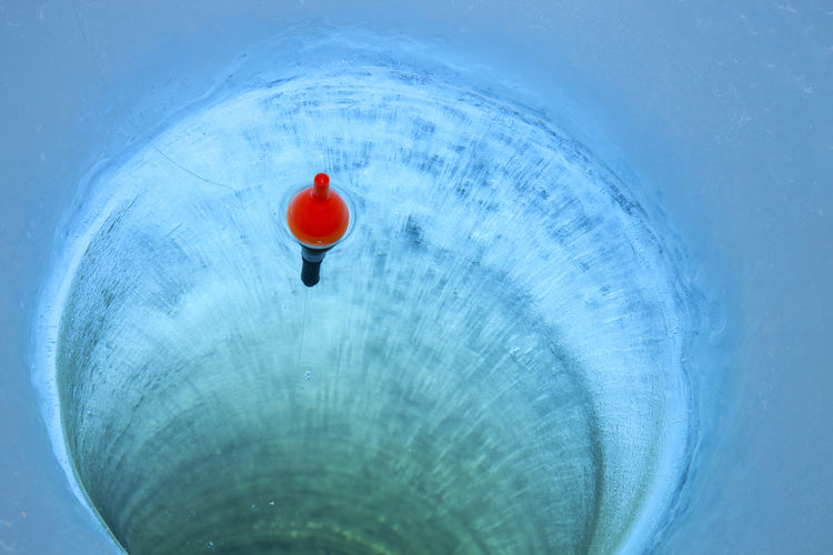 Red bobber and fishing line in an ice fishing hole in a minnesota lake