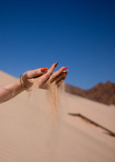 Cropped hand of woman on sand at desert