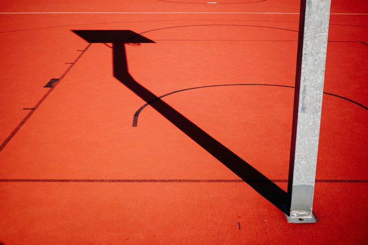 Shadow of basketball hoop on red court during sunny day