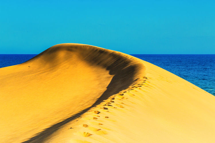 Scenic view of curvy sand dune against clear blue sky at maspalomas 