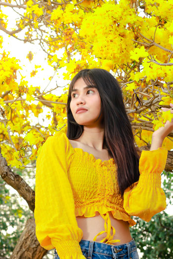 Portrait of beautiful young woman standing against yellow autumn tree