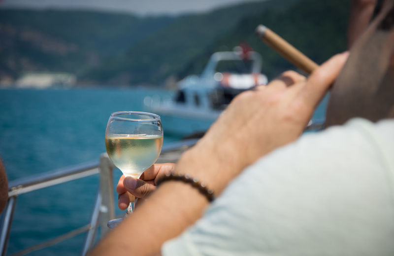 Close-up of hand holding wineglass over river against sky