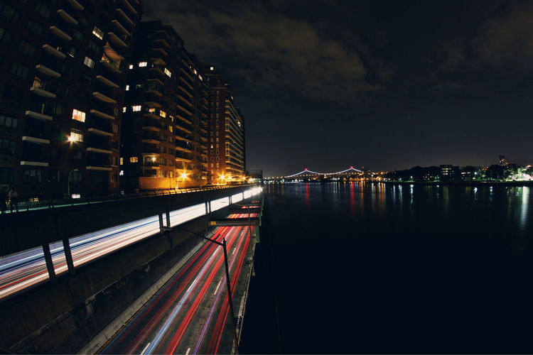 Light trails on bridge by river in city at night