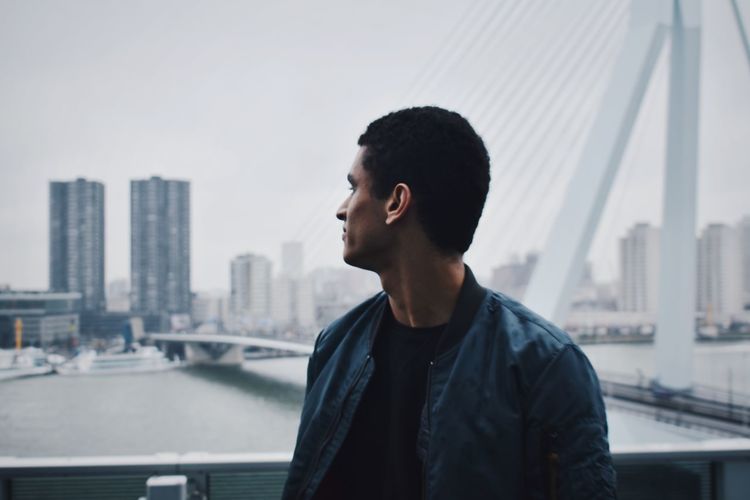 Young man looking at city while standing against bridge