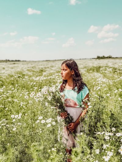 Cute girl holding plants standing in field