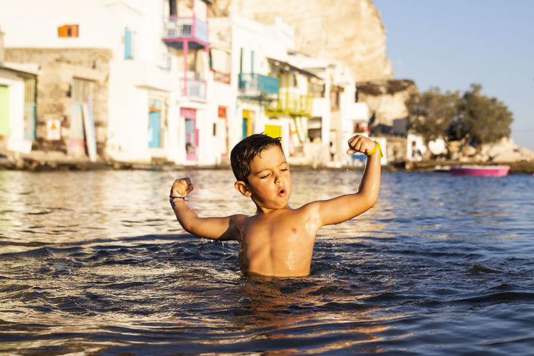 Shirtless boy flexing muscles in sea