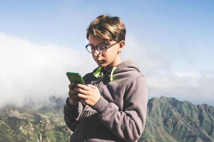 Boy using mobile phone while standing against mountain range