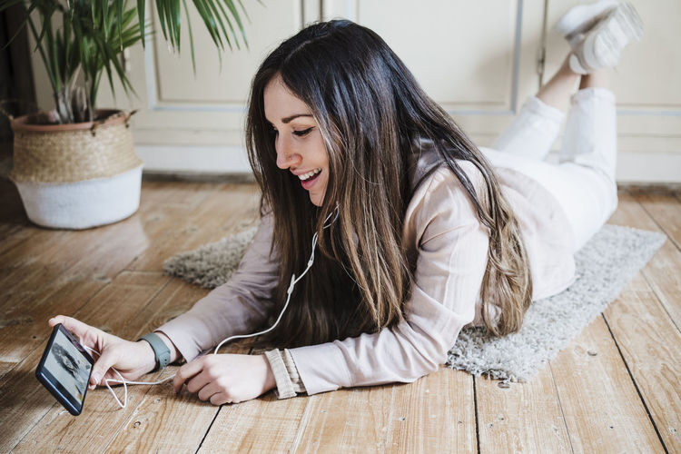 Young woman using phone while sitting on floor at home