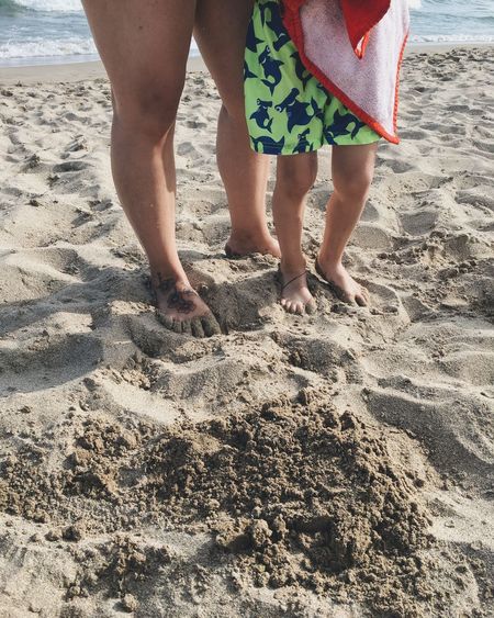 Low section of boy with mother standing on sand at beach