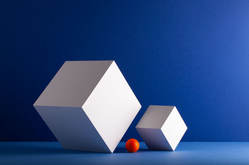 Two cubes with orange golf ball on the blue background