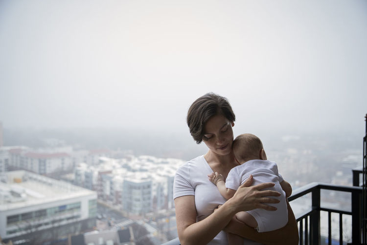 Mother carrying son while standing in balcony during foggy weather