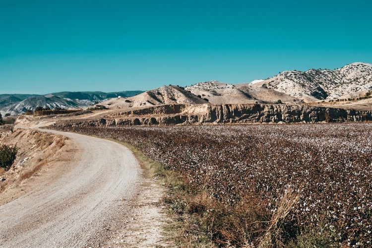 Dirt road on landscape against clear blue sky