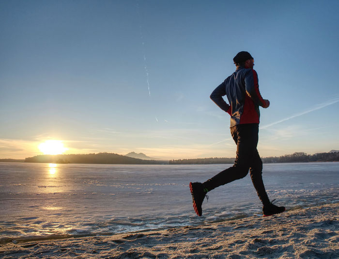 Winter training. runner in winter landscape with blue sky sunset over the frozen lake