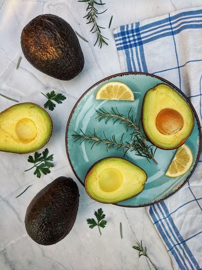 Fresh avocado with herbs and lemons lies on the table on blue plate on white background. flat lay