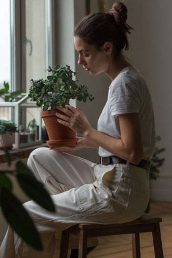 Young woman gardener taking care of green home plant in pot. home gardening, love of houseplants.
