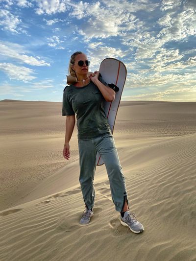 Full length of woman holding sandboard at desert during sunset