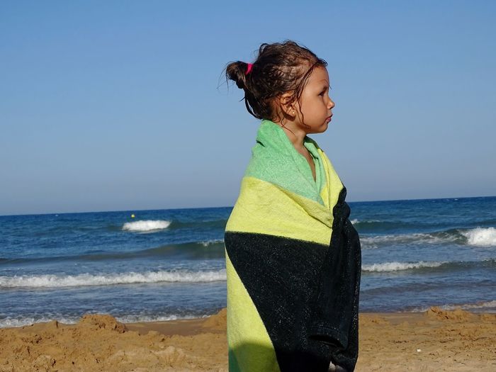 Boy standing on beach against clear sky