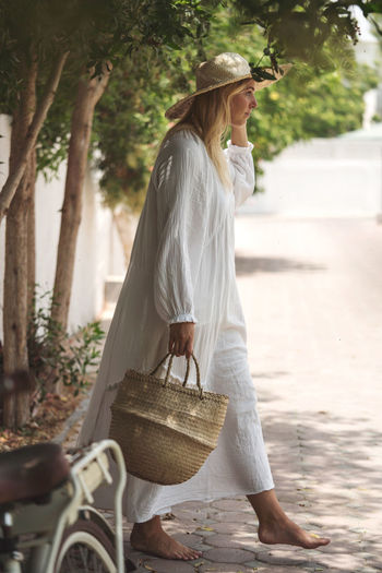 Woman wearing white dress walking in the garden barefoot