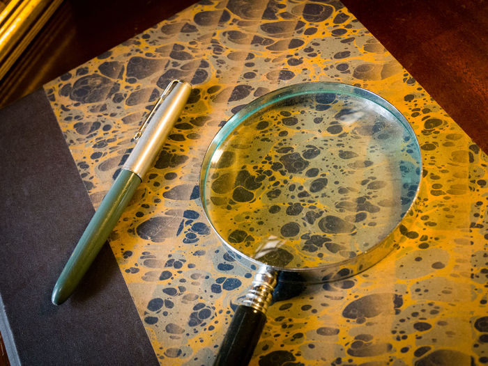 High angle view of pen and magnifying glass on book