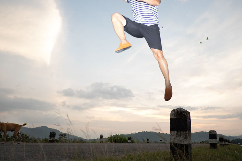 Low section of man jumping against sky