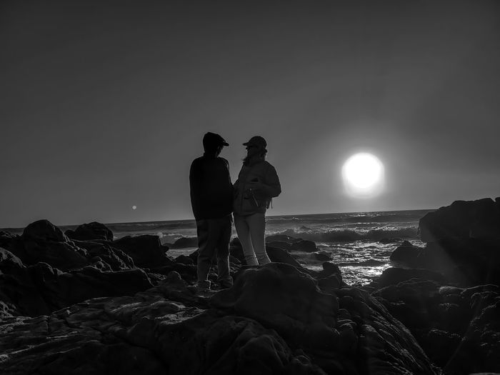 Man and lady standing on rock at beach against sky