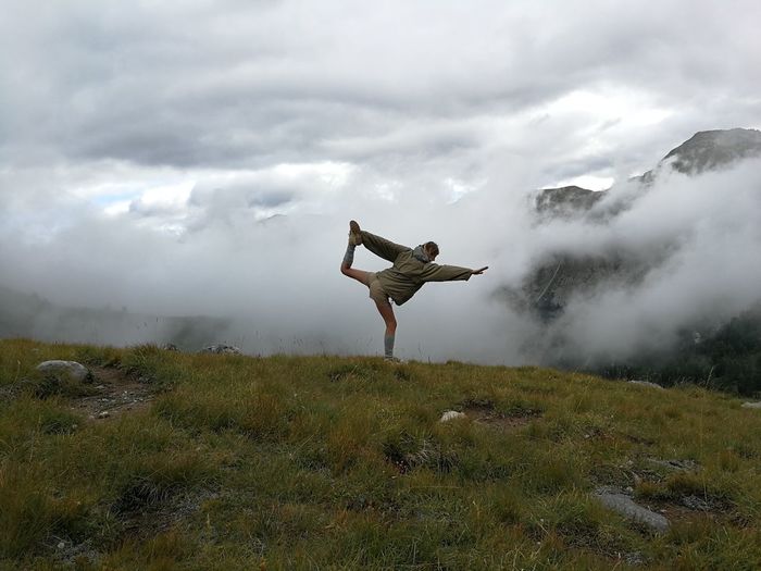 Woman exercising on mountain against sky