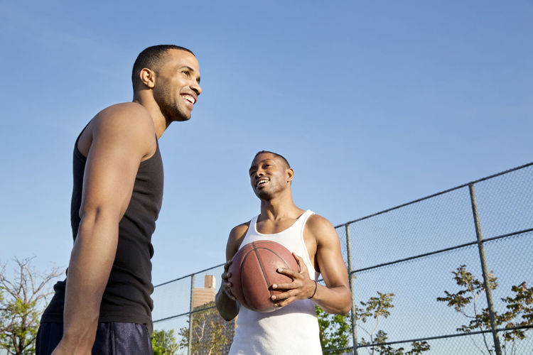 Low angle view of happy basketball players while standing in court against clear sky