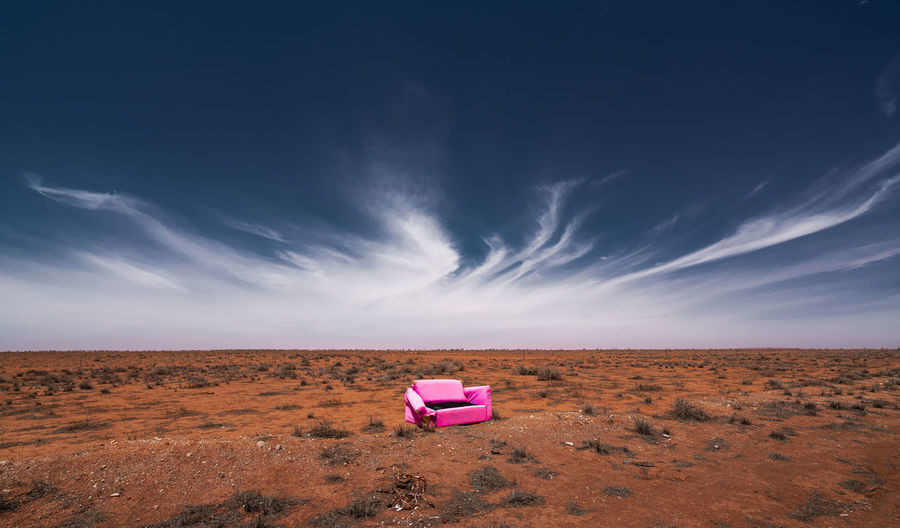 Pink umbrella on desert land against sky