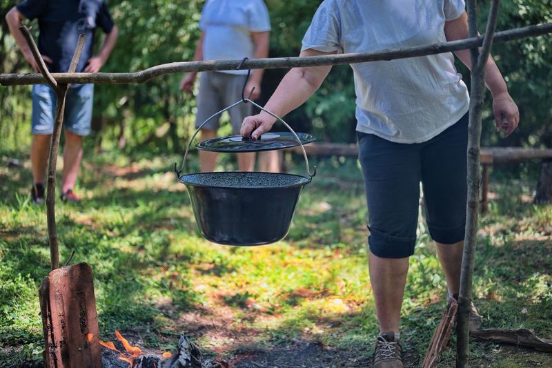 Midsection of woman preparing food on campfire in nature