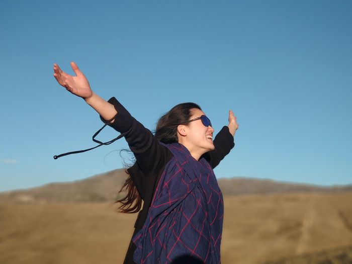 Woman with arms outstretched standing against sky