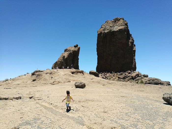Full length of boy walking on rock formation against clear blue sky