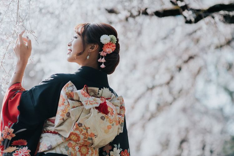 Low angle view of woman in kimono standing by cherry blossoms