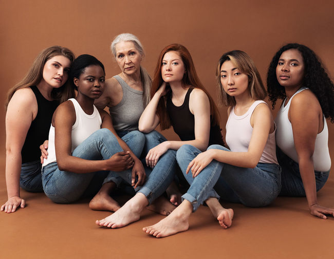 Multi-ethnic women sitting against brown background