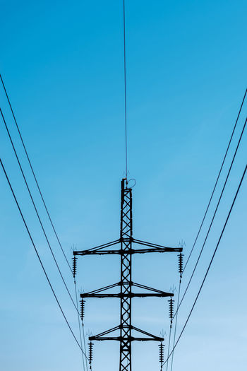 High voltage electricity transmission metallic tower pole dark silhouette in blue evening sky