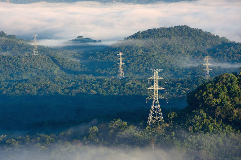 Transmission tower in green forest and morning smooth fog. energy and environment concept. 