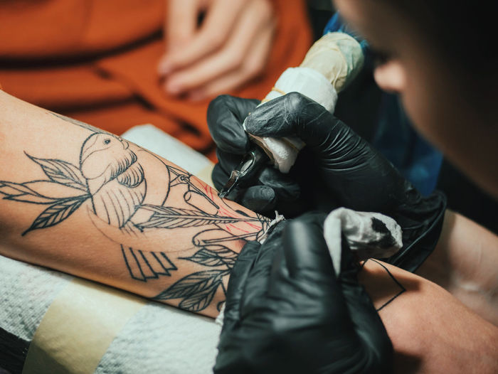 Cropped image of female artist making tattoo on male customer hand