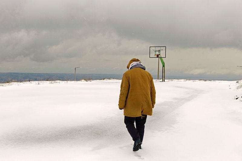 Full length rear view of man walking on snow covered landscape