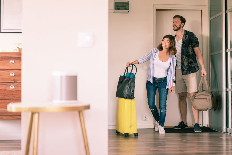 Full length of couple with luggage looking around in apartment while standing at doorway