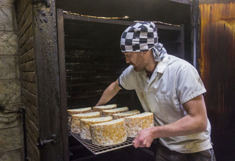 Manual worker inserting stilton cheese tray in smokehouse at food factory
