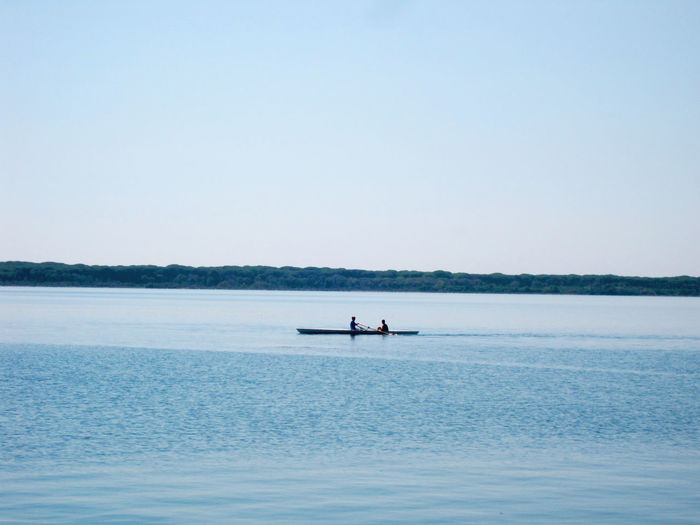 People sitting in boat on sea against clear sky