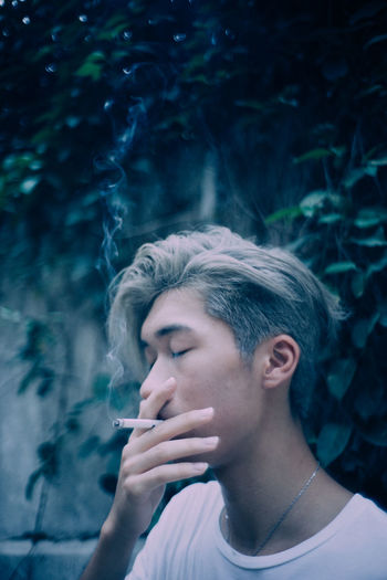 Close-up of young man smoking cigarette against plants