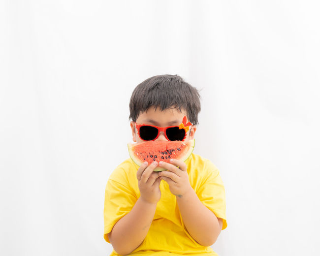 Portrait of boy wearing sunglasses while having watermelon against white background