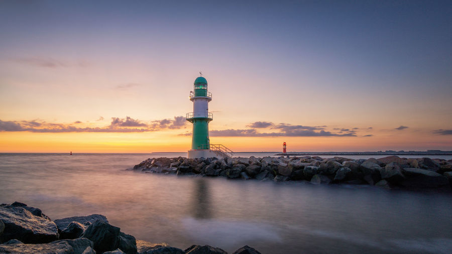 Lighthouse by sea against sky during sunset