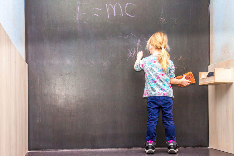Full length of girl writing on blackboard