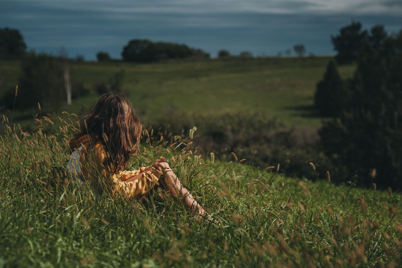 Tween girl looking away at a green hillside with dark skys