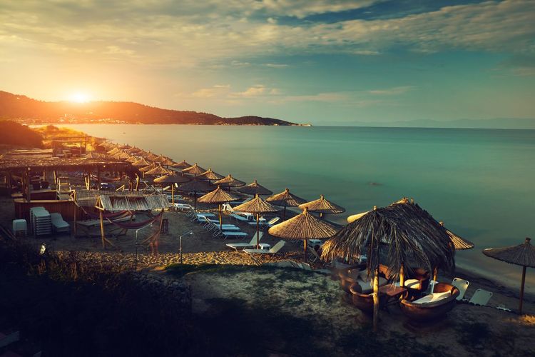 Parasols and chairs arranged at beach against sky during sunset