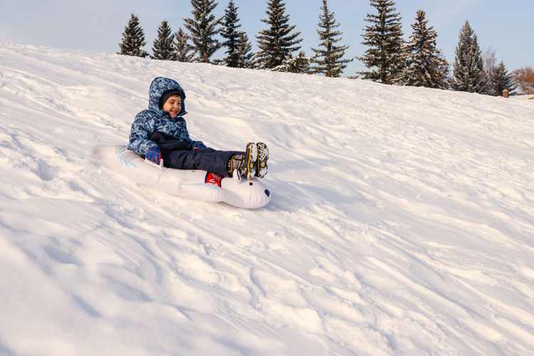 Young boy sliding down a snowy hill on a toboggan