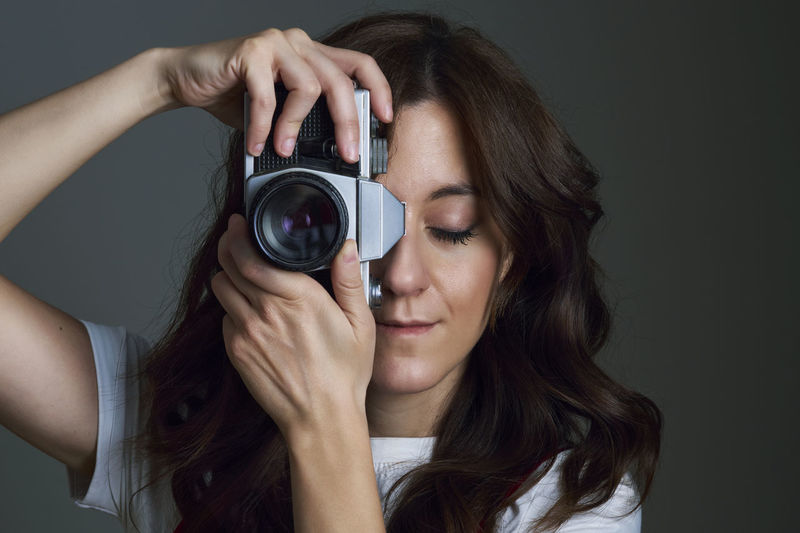 Close-up portrait of woman holding camera over black background