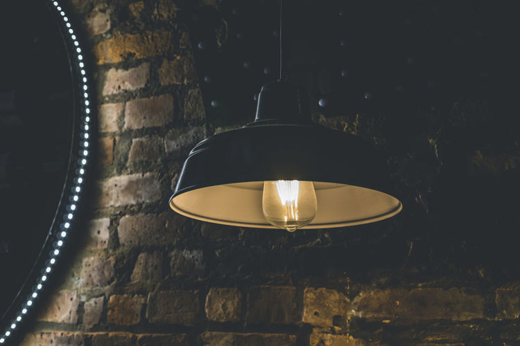 Vintage lamp with light bulb hanging against red brick wall in the darkness